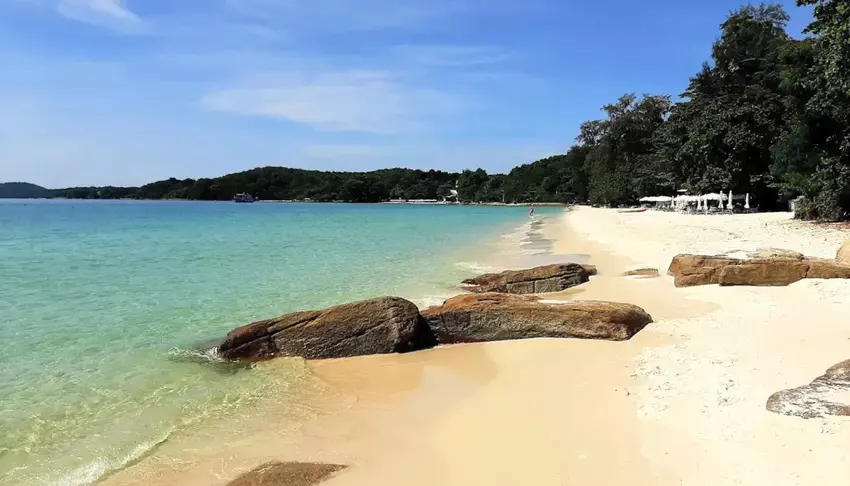 Береговая линия белоснежного пляжа с несколькими камнями и зеленью